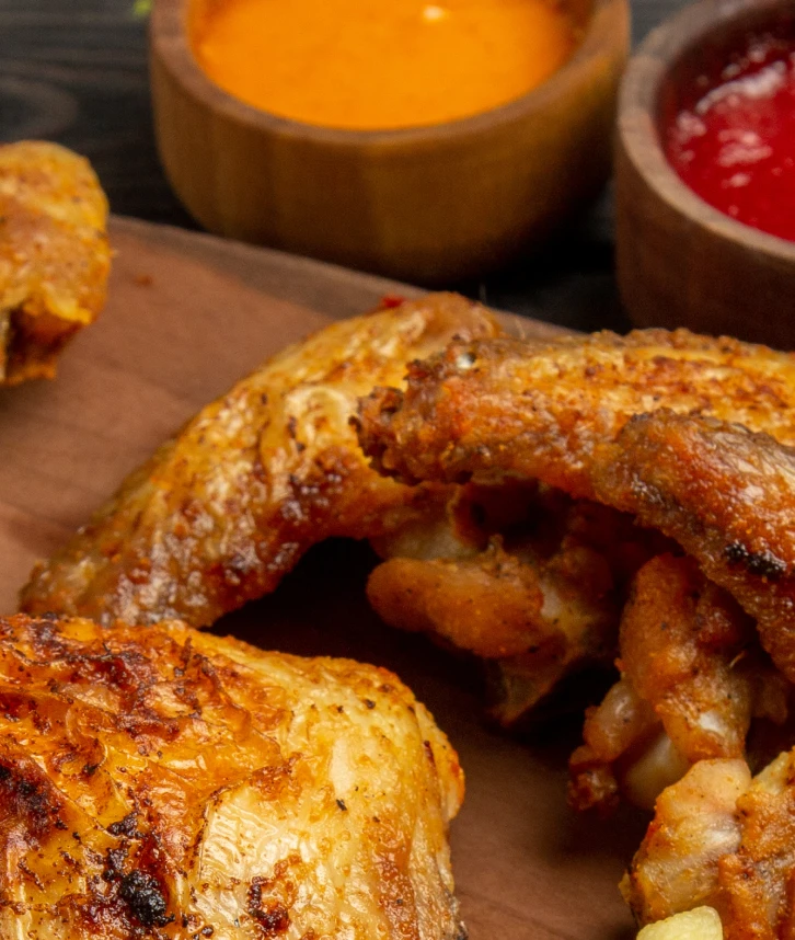 Des morceaux de poulet rôti dorés et croustillants servis sur une planche en bois, accompagnés de deux sauces dans des bols en bois, une orange et une rouge.