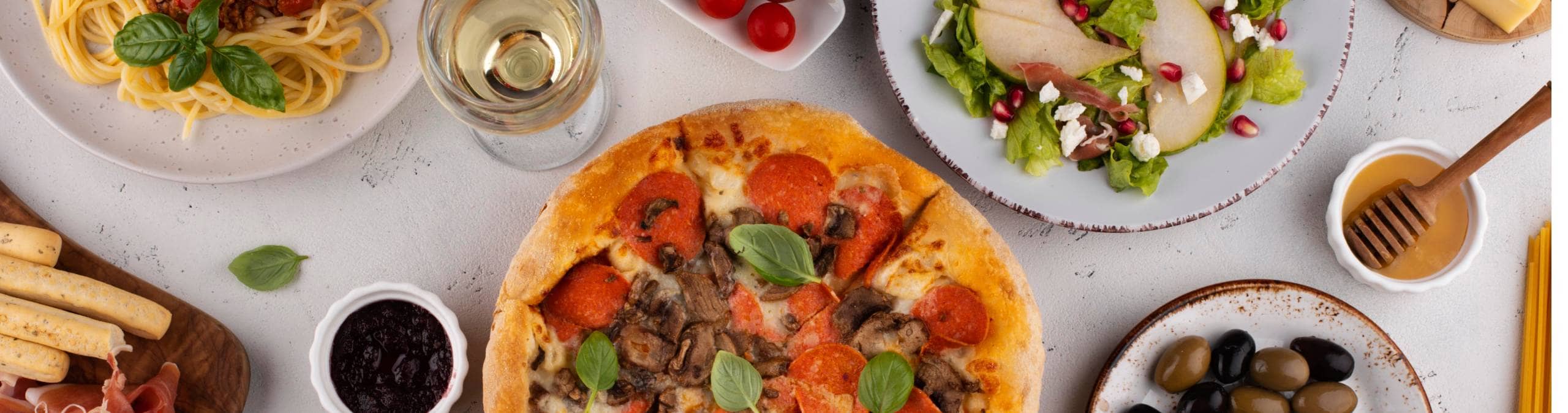 Vue de haut d'un table contenant de la pizza, du spaghetti, des olives, du poulet, etc.